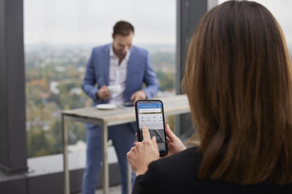 Frau sucht mithilfe ihres Smartphones und der SAUTER App einen Kollegen