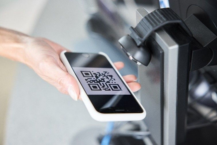 Person hält ein Smartphone, auf dem ein QR-Code zu sehen ist, unter ein Lesegerät